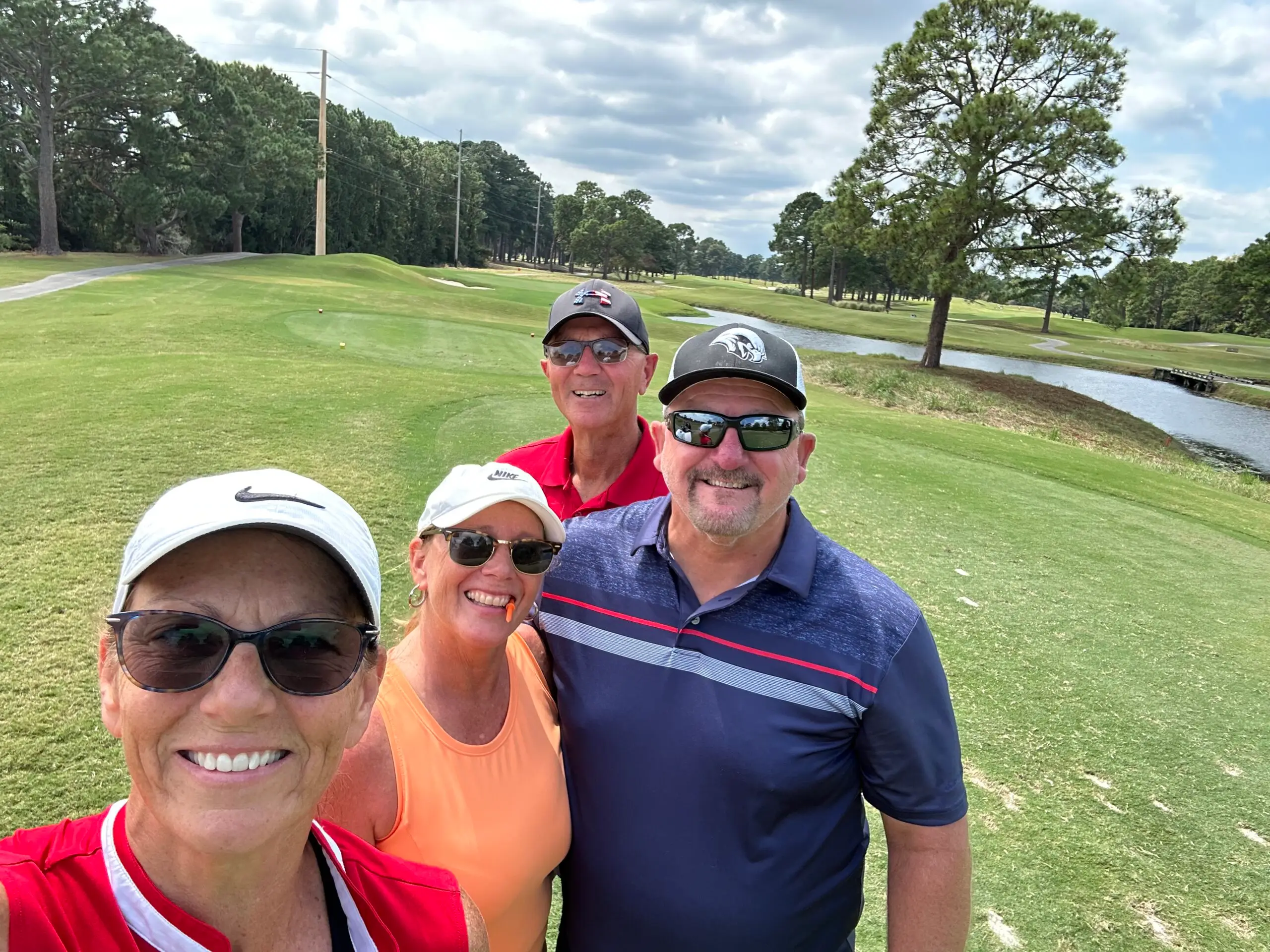 Four golfers standing together beside a fairway and creek