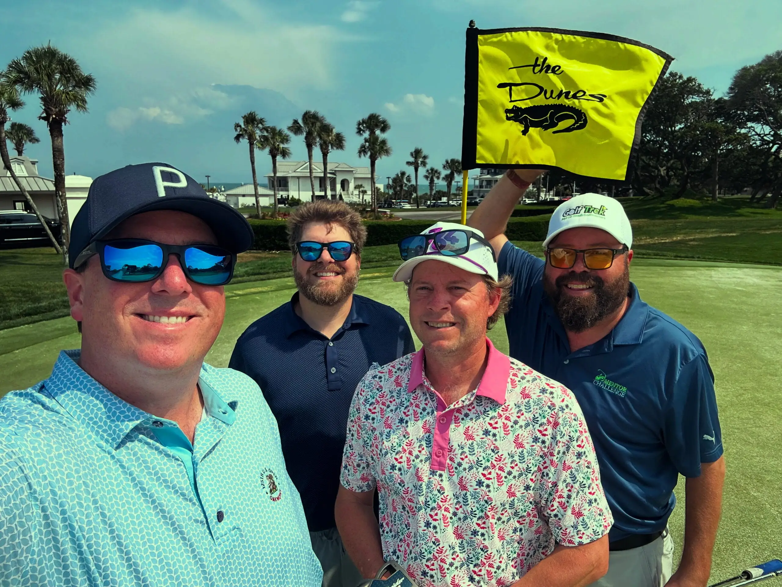 Foursome posing with the flag on a green at The Dunes Club