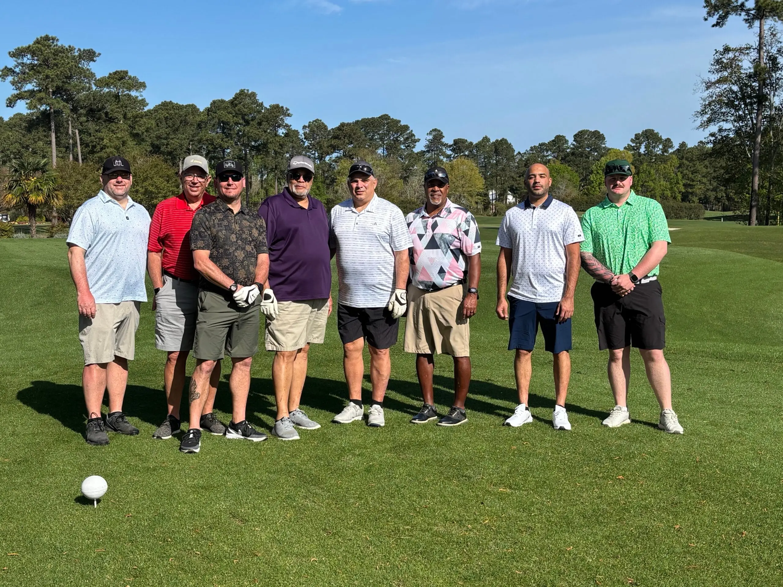 Eight golfers lined up on the tee box on a clear spring morning
