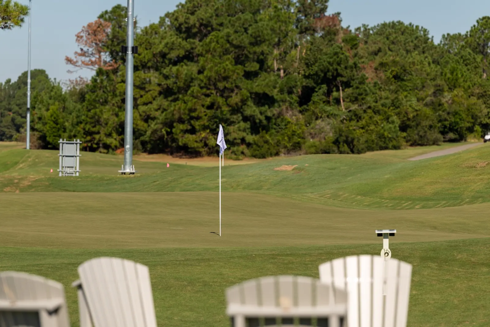 White Adirondack chairs in the foreground looking out over a Piper green with a flag and a light pole beyond