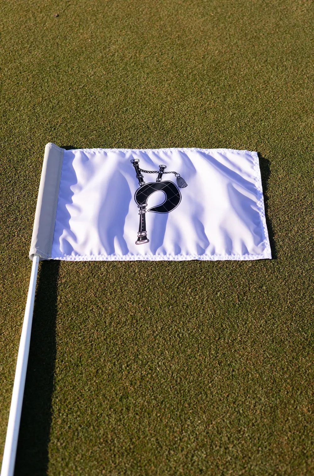 A white Piper flag with a bagpipe logo lying on a close mown green