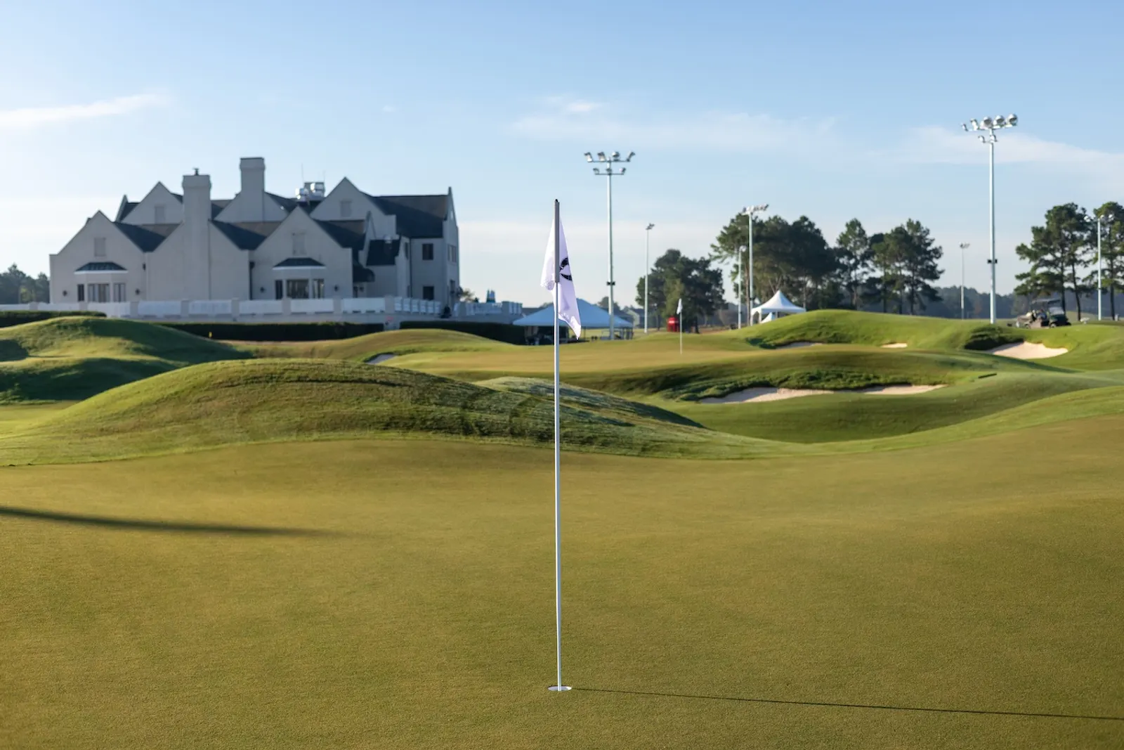 A green on The Piper with a white flag, surrounded by mounding and a bunker, with the Legends clubhouse and light poles behind