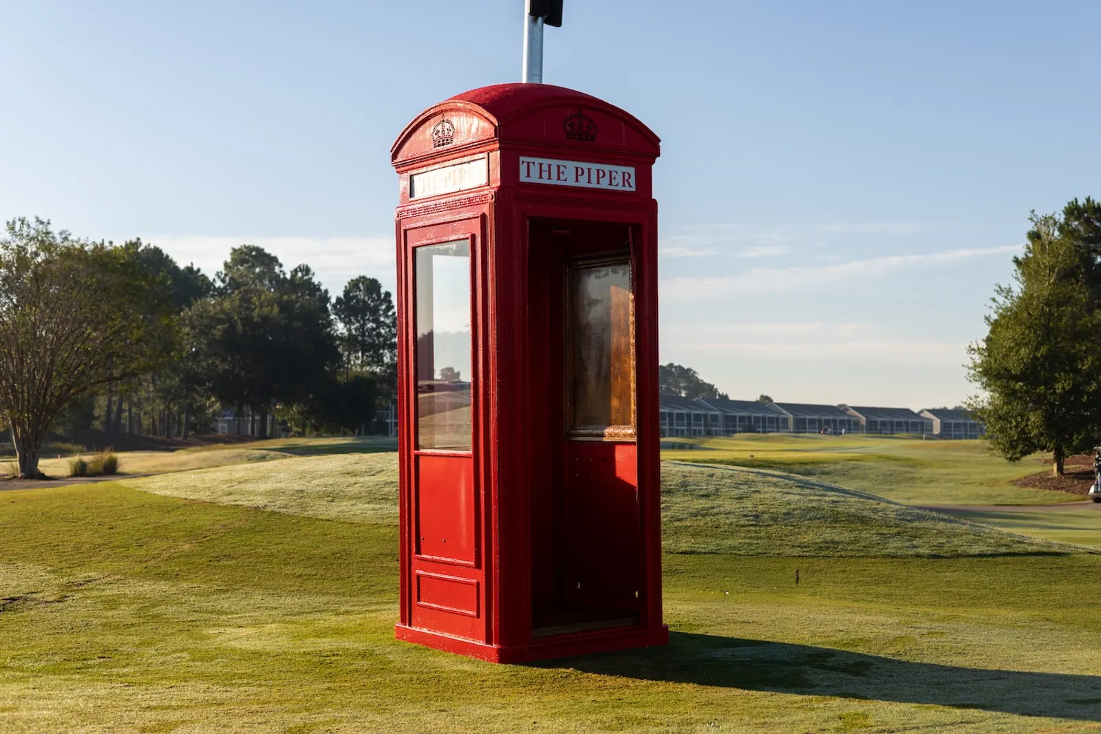 A bright red British telephone box lettered The Piper standing on a tee at Legends Golf Resort in early morning light