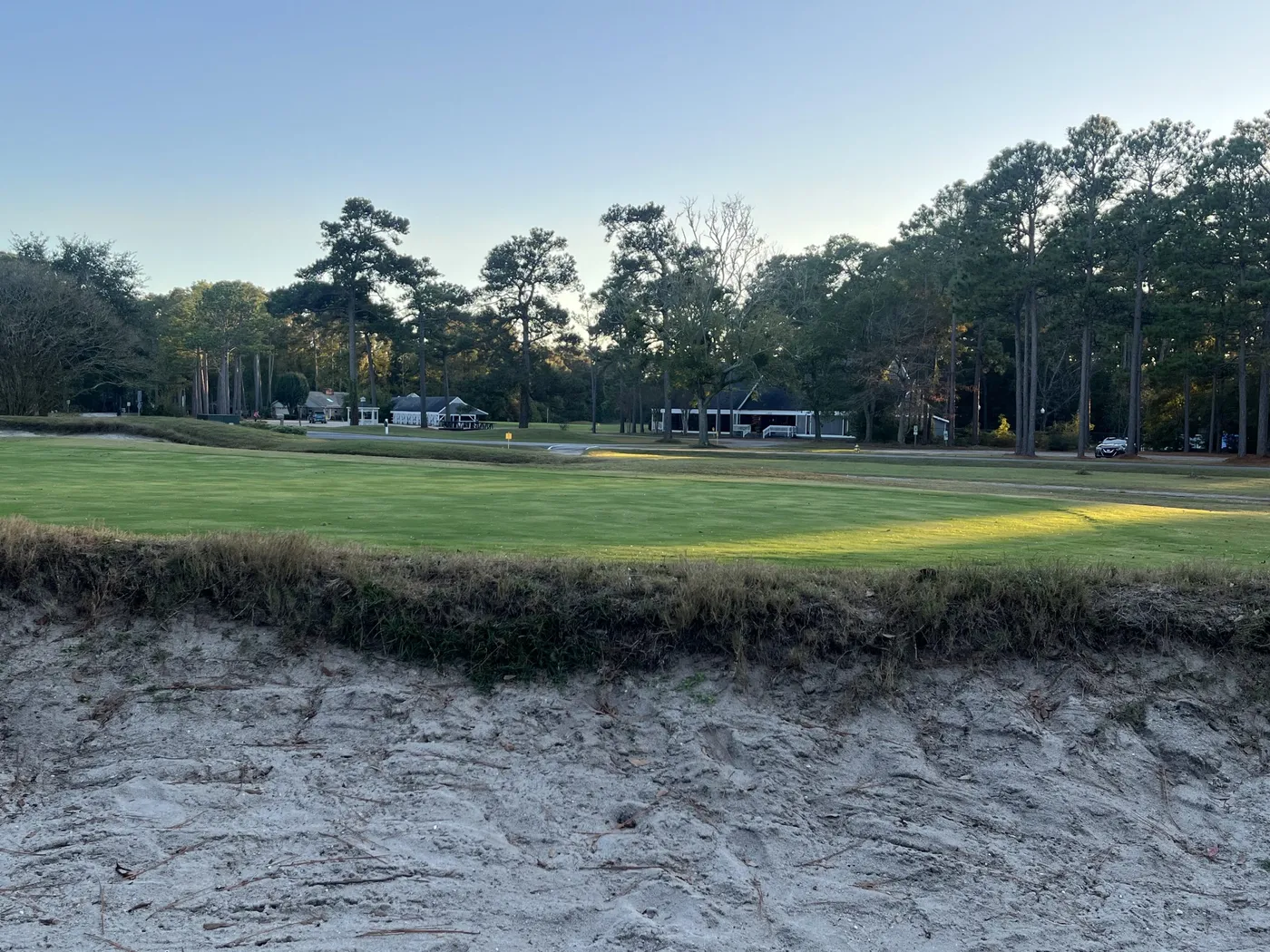 A fairway and clubhouse at the closed Carolina Shores Golf and Country Club seen from an unraked bunker