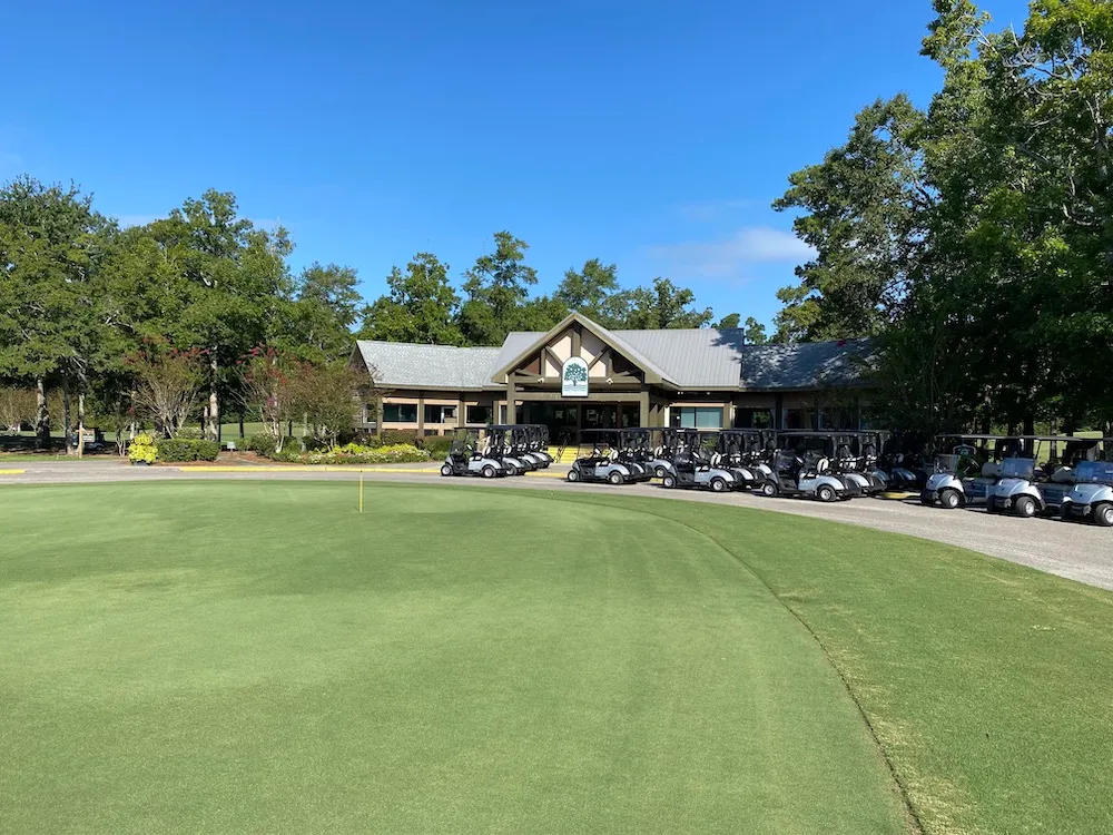 Golf carts lined up in front of the River Oaks Golf Club clubhouse on a sunny morning